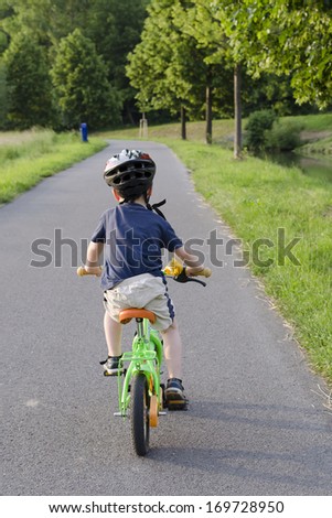 Child cycling on a cycle path in nature, back view.
