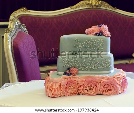 Luxury wedding cake decorated with pink roses on table; antique furniture in background.