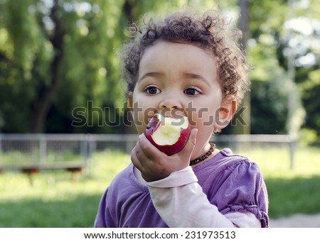 Child girl eating an apple in a park in nature.