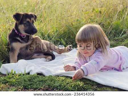 Child girl with puppy dog relaxing on blanket in grass at nature meadow.