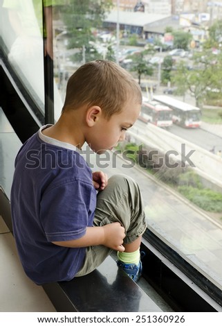 Child boy looking from a large window, watching traffic on a street below.