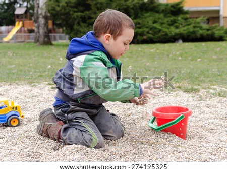 Child playing with toy digger and stones pebbles in playground park.
