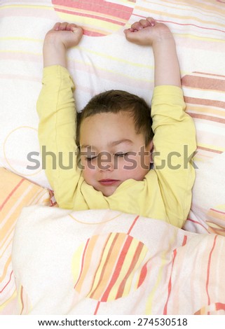 Sleepy child lying in a bed, waking up and stretching  in the morning.