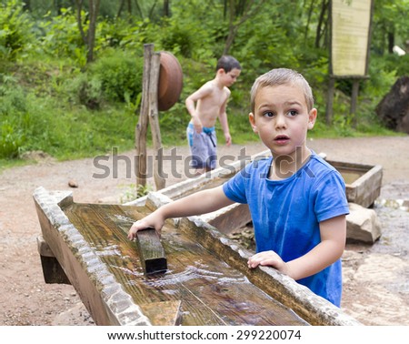 Children playing with water in wooden fountain in park or natural playground