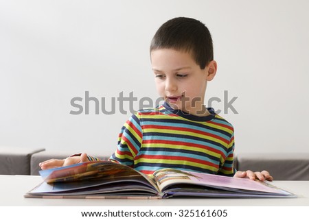 Child boy reading a large picture book at a desk or table book