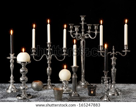 burning candles on silver candle holders on black background