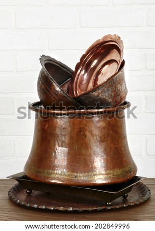 some copper ware in big cauldron on table in font of white, brick wall