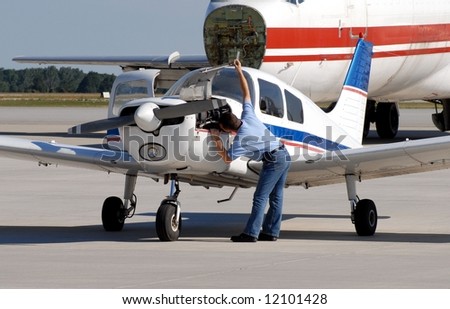 mechanic inspecting a small engine aircraft, larger Airplane in background