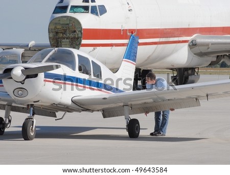 aircraft mechanic inspecting a small engine aircraft, larger Airplane in background