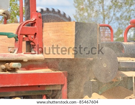 cutting lumber on an outdoor band saw, sawdust flying flying around