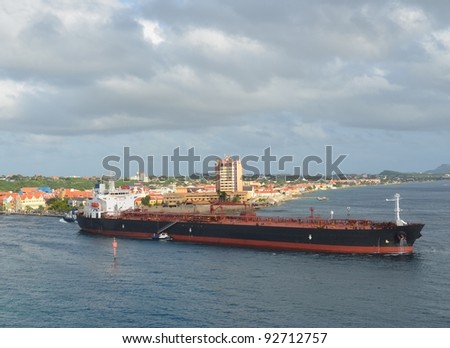 Tanker ship escorted by Pilot boat leaving Port of Willemstad , city in the background; Curacao