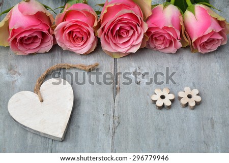 Row of pink yellow roses with label and heart shape decoration on a old wooden grey background