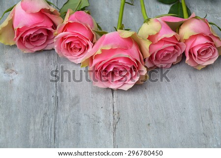 Row of pink yellow roses with label and heart shape decoration on a old wooden grey background