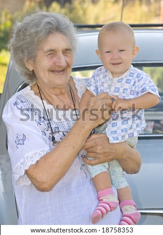 The old grandmother holds the little grand daughter and smiles. Shallow DOF.