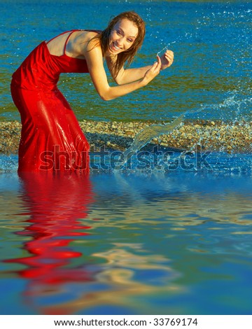 The girl in red dress fun, splashing in the river on a hot day