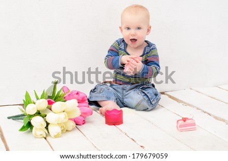 boy sitting on the wooden floor of  white planks, with gifts and flowers for mom
