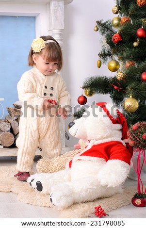 toddler girl with big teddy bear at christmas tree indoors