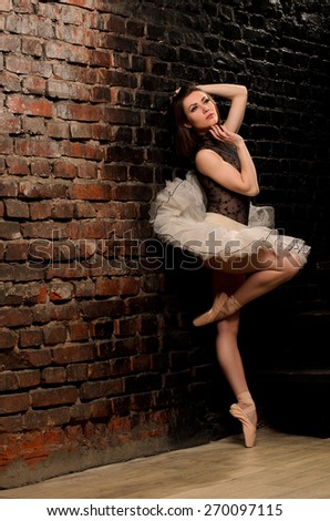 ballerina in tutu on tiptoe near old brick wall