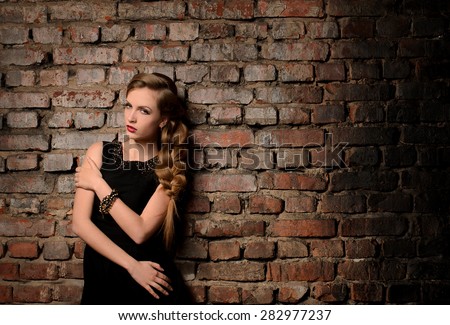 young attractive woman with thick braid in black gown on old brick wall background