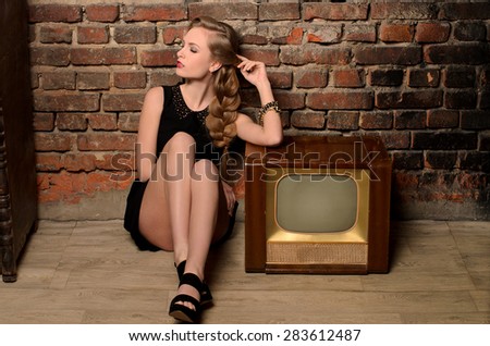 young sensual woman sitting on floor near retro tv set on old brick wall background