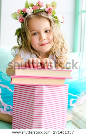 little cute girl with curly hair covered with wreath and pink books indoors