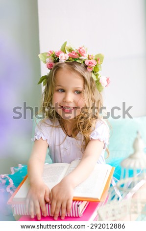 little smiling girl with curly hair covered with wreath and books indoors