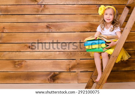 little cute girl with curly hair holding stack of books and sitting on stairs of ladder on brown wooden wall background with space for text