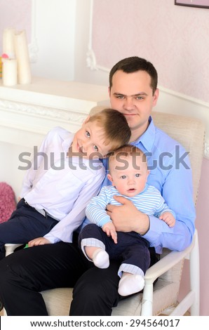 young daddy and two little sons sitting on armchair indoors