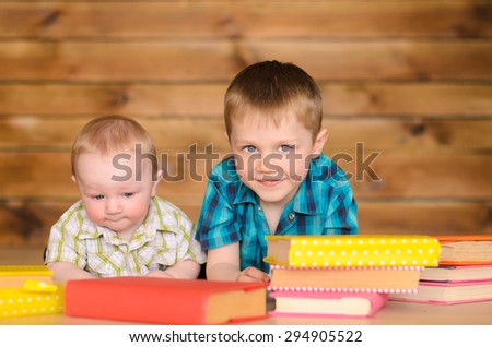 elder and younger little boys with colored books on brown wooden wall background