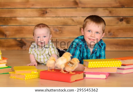 elder and younger little boys with colored books and alive chickens on floor on brown wooden wall background
