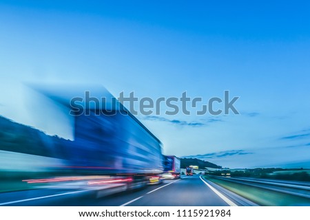 Background photograph of a highway in night. Trucks drive on a highway, motion blur and light trails. Evening or night shot of trucks, transportation, logistics on a highway or freeway.
