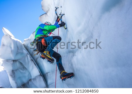 Epic shot of an ice climber climbing on a wall of ice. Mountaineer and climber on an adventure extreme ascent with ice axe and crampons. Alpine extreme climbing on a serac or crevasse.