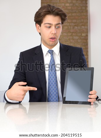 Businessman pointing to the blank screen of a tablet computer visible to the viewer in horror and stupefaction with his mouth open