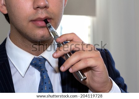 Close up view of the hand and mouth of an anonymous businessman with an e-cigarette in his hand about to place it in his mouth for a smoke
