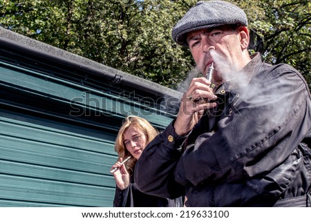 Man and woman standing smoking e-cigarettes outdoors with a lowe angle view off the middle-aged man exhaling smoke from his nostrils in the foreground