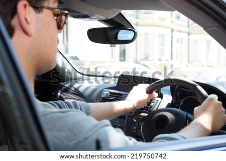 View through the side window of a young man driving a car in an urban environment
