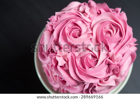 Overhead view of a freshly baked cake decorated with pink icing sugar roses displayed on a cake stand over a black background with copyspace