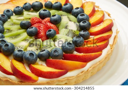 Close up Fresh Berry, Apple and Kiwi Fruits on Top of a Tasty Cake with Frosting, Served on a White Plate.