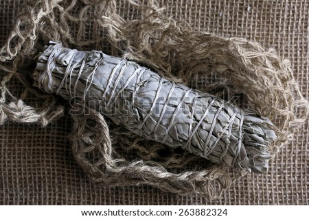 Dried Sage\
White sage smudge stick or bundle of dried sage wrapped with string on burlap and twine background.