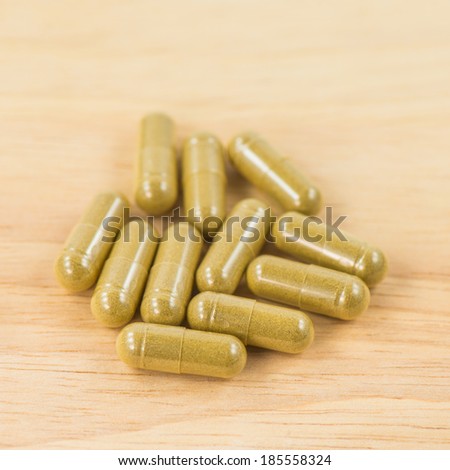 Herbal pills in transparent cup over wood background