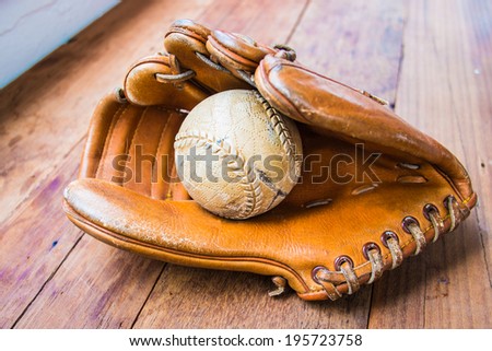 Old worn leather baseball glove and used ball on wood table