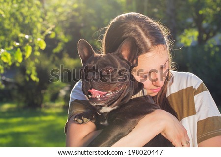 Girl holding a French bulldog in her arms.