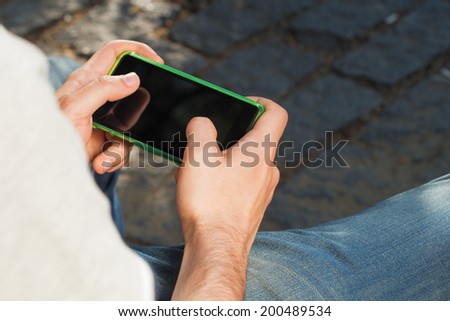Man typing messages on his smart-phone while sitting on a park bench.