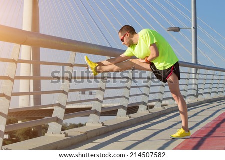 Urban jogger on a big bridge, stretching after running.