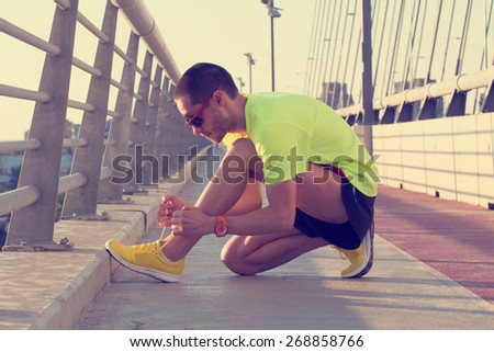 Urban jogger tying his running shoes on a big bridge.