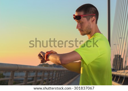 Urban jogger on a big bridge checking his running time. focus on the watch and hands.