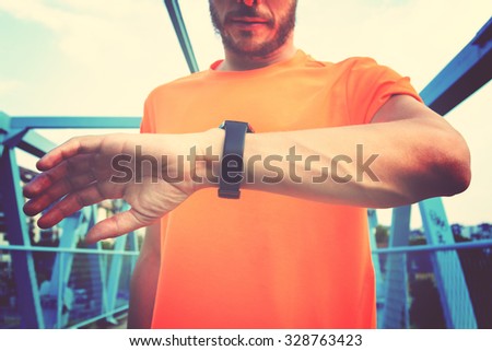Urban jogger on a big bridge checking his running time. Focus on the watch and hands.