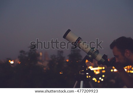 Man looking at the stars with telescope with de-focused city lights.