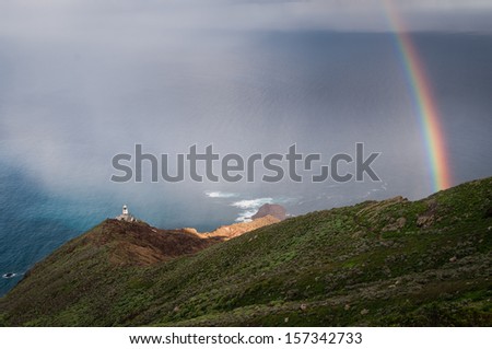 Picture of small lighthouse with colorful rainbow created by heavy rain on the ocean.