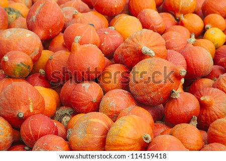 A pile of pumpkins that are piled up near a street so people can take them and leave money in a cash box.